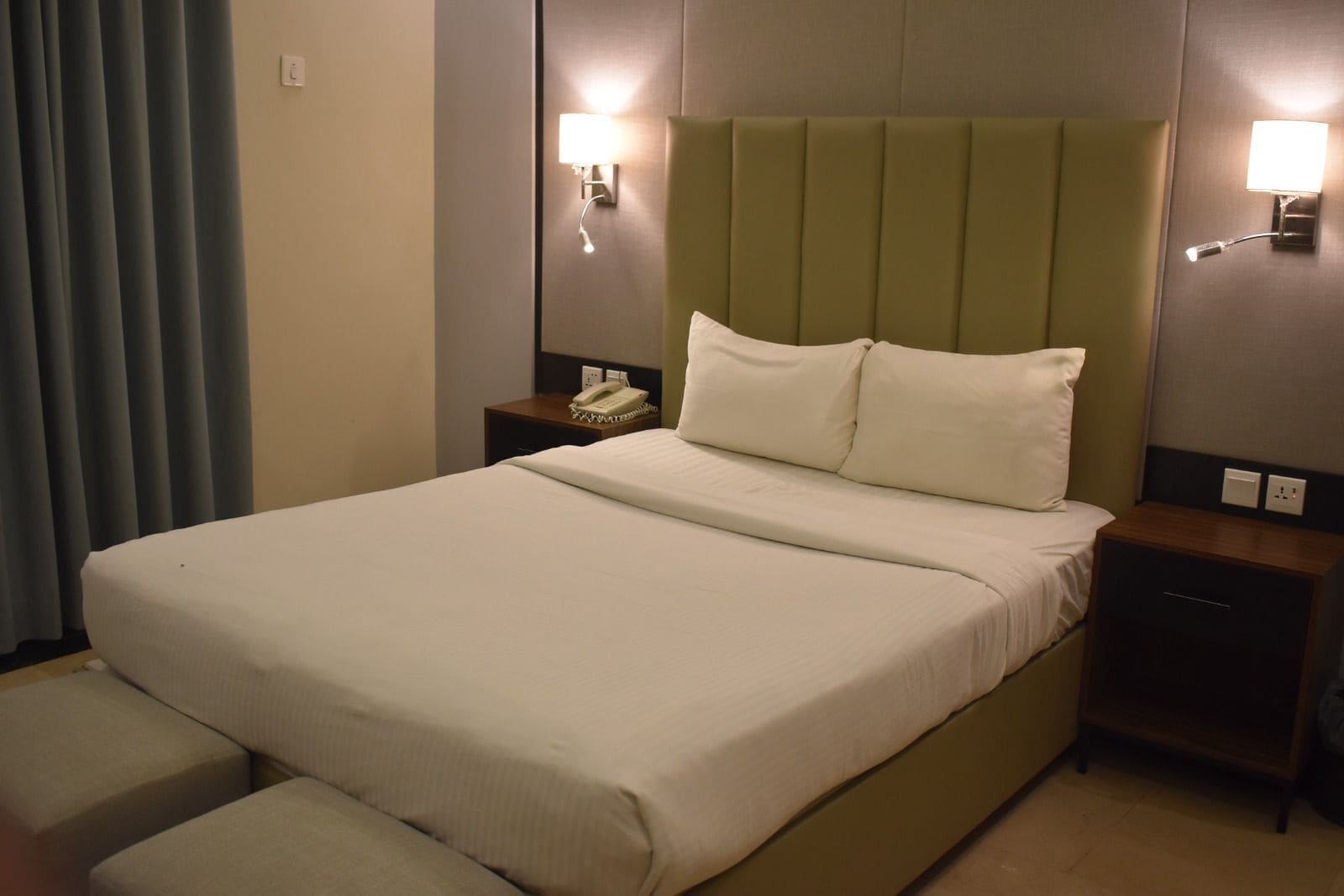 Habitación de hotel con una cama grande, dos mesitas de noche, un teléfono y dos lámparas de pared.