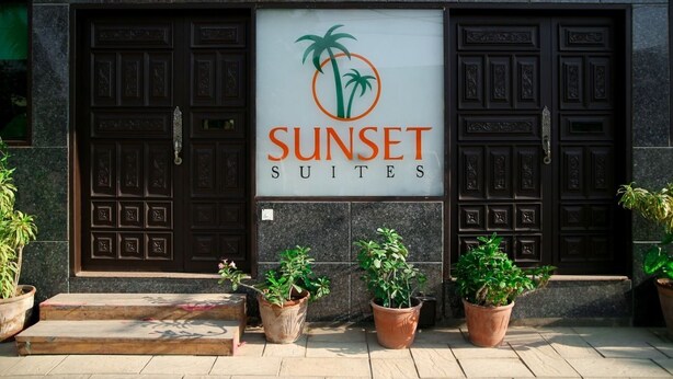 A building entrance with a sign reading "SUNSET SUITES" and two large wooden doors.