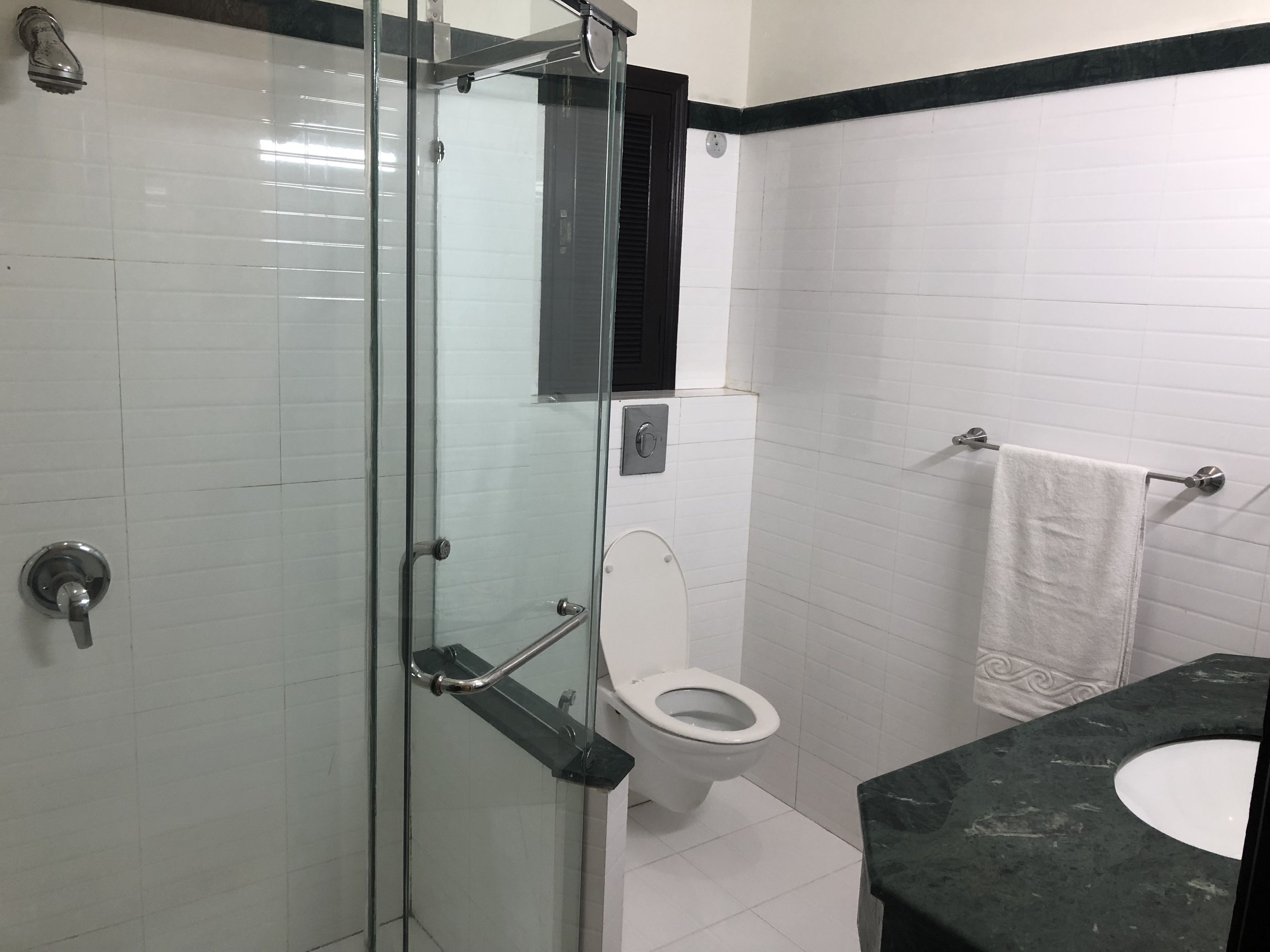 Une salle de bain avec une douche à parois de verre, des toilettes blanches, un miroir à cadre noir et un lavabo en marbre.
