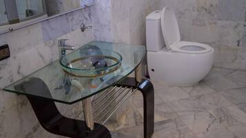 Un baño con lavamanos de vidrio, inodoro blanco y suelo de mármol.
