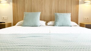 Ein Hotelzimmer mit einem Holzkopfteil, zwei Kissen mit geometrischem Muster, einer weißen Bettdecke und einem Nachttisch mit einer Lampe.