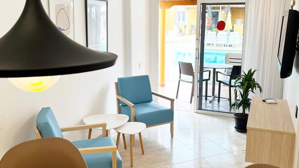 Ein modernes Wohnzimmer mit Sofa, Sesseln, einem Couchtisch und einem Essbereich mit Tisch und Stühlen. Ein großes Fenster bietet Blick auf einen Pool und Sitzmöglichkeiten im Freien.