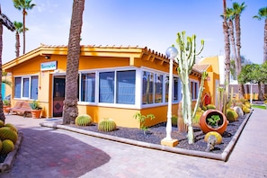 A reception area with a yellow building, large windows, and a cactus garden. - Los Almendros (San Bartolome de Tirajana)