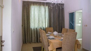 Comedor con una mesa dispuesta para cuatro personas, sillas, una araña y cortinas.