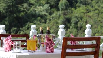 A table set outdoors with a white tablecloth, a bottle of champagne, a pitcher, and a glass of orange juice.