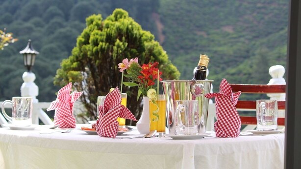 A table set with a bottle of champagne, a pitcher, and glasses, with a scenic mountain view in the background. - Hotel Silverfalls (Nuwara Eliya)