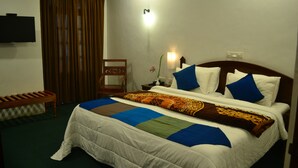 A neatly made bed with a white comforter and blue and brown decorative pillows. A wooden bench is visible to the left of the bed. - Hotel Silverfalls (Nuwara Eliya)