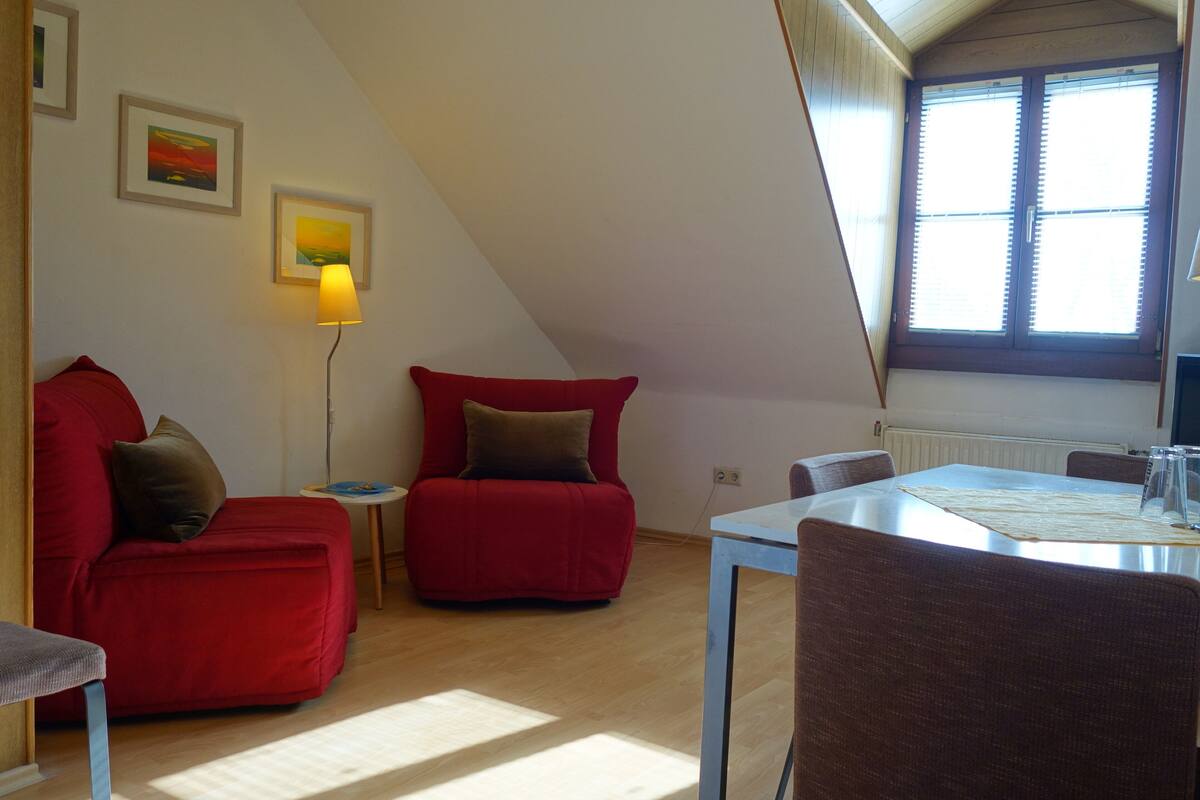 A cozy room with a red sofa, a small table, and a dining table with chairs.