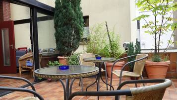 Eine Terrassenfläche mit Korbstühlen, runden Tischen und Blumentöpfen.
