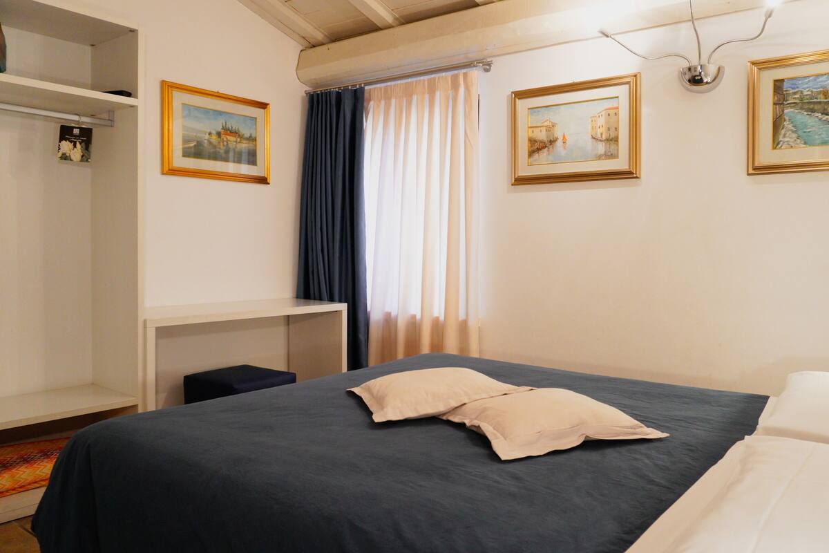 A bedroom with a bed, a desk, and two framed paintings on the wall.