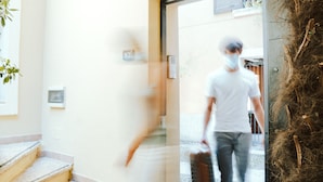 A person walking through a doorway carrying a suitcase.