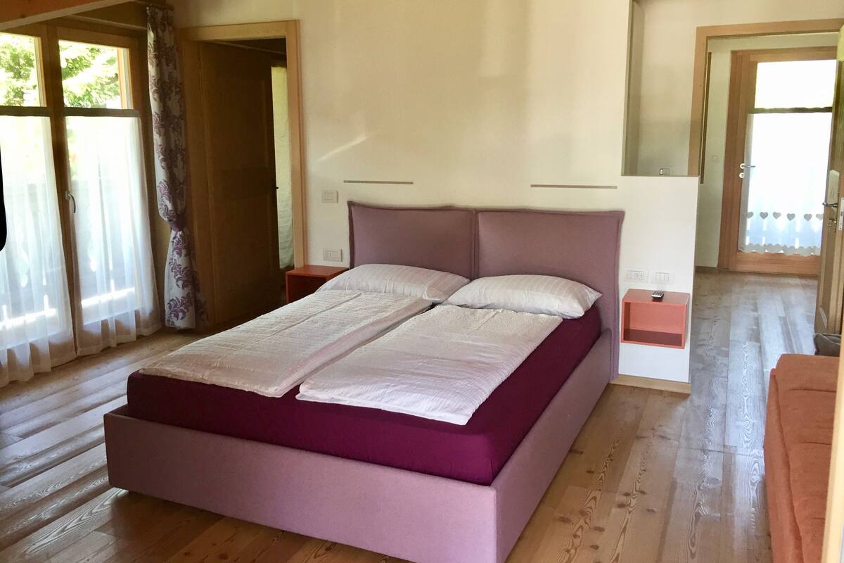 Une chambre à coucher avec un lit, un plancher en bois et une fenêtre avec des rideaux.