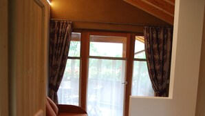 Een compacte kamer met een houten vloer, een bed, een klein zitje en een raam met gordijnen.
