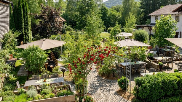 Un patio al aire libre con mesas y sillas, rodeado de follaje y árboles.