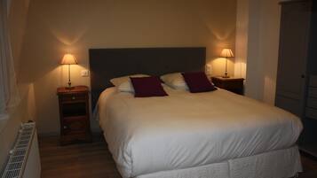 Una cama bien tendida con ropa blanca y dos almohadas rojas, con dos lámparas de noche de madera a cada lado.
