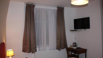 Una habitación de hotel con una cama, un escritorio, un televisor y un ventanal con cortinas.
