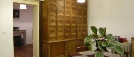 Un comedor con un armario de madera, una mesa con mantel, sillas y una planta en maceta.