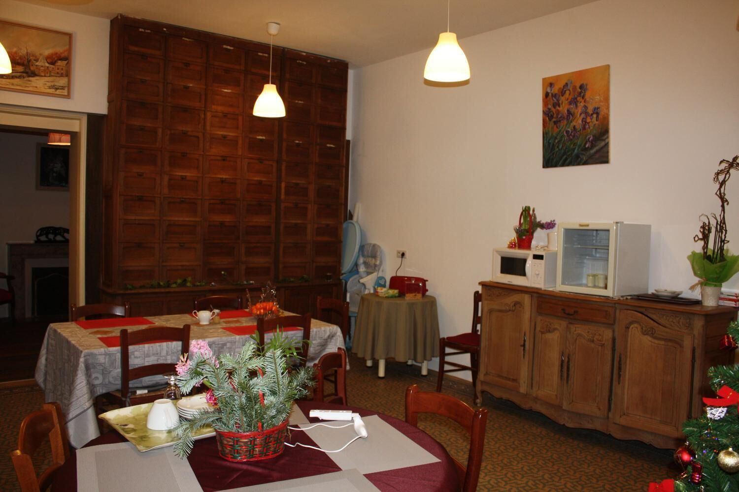 A dining area with a wooden cabinet, a table with a red tablecloth, and a Christmas tree.