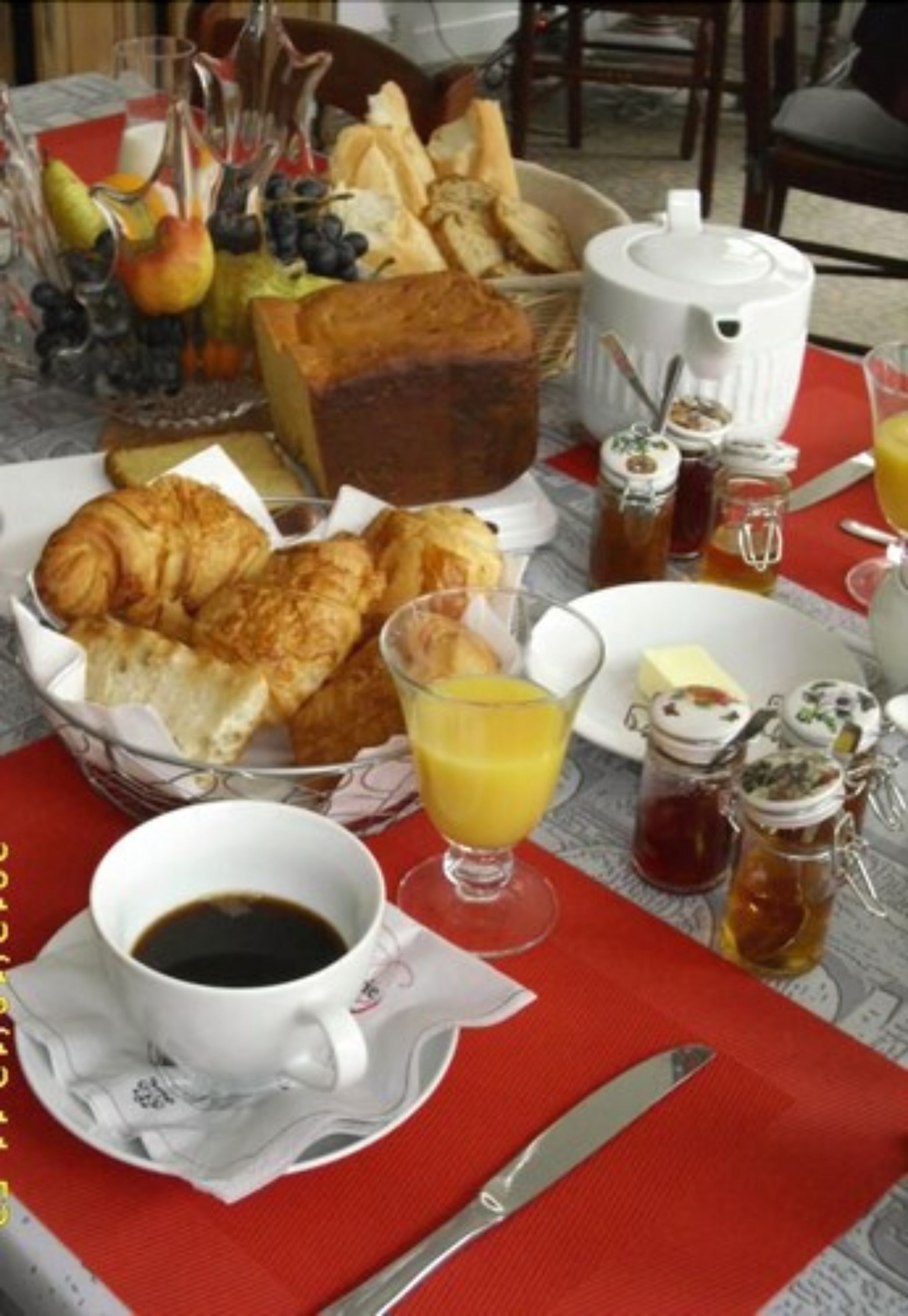 Ein Frühstückstisch mit Croissants, Brot, einer Kaffeekanne, einem Glas Orangensaft und verschiedenen Beilagen.
