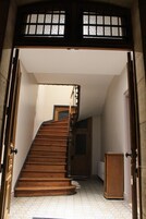 Una escalera de madera que sube a un piso superior, con una puerta arriba y un radiador abajo.