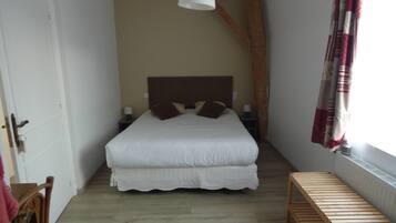 A bedroom with a large bed, a wooden bench, a hanging light fixture, and a window with curtains.