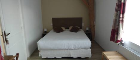 Un dormitorio con una cama grande, un banco de madera, una lámpara colgante y una ventana con cortinas.