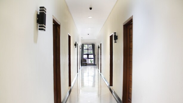 A long, well-lit hallway with a shiny tiled floor, wooden doors, and wall-mounted light fixtures. - Hotel O Cempaka Place Homestay (Jakarta)