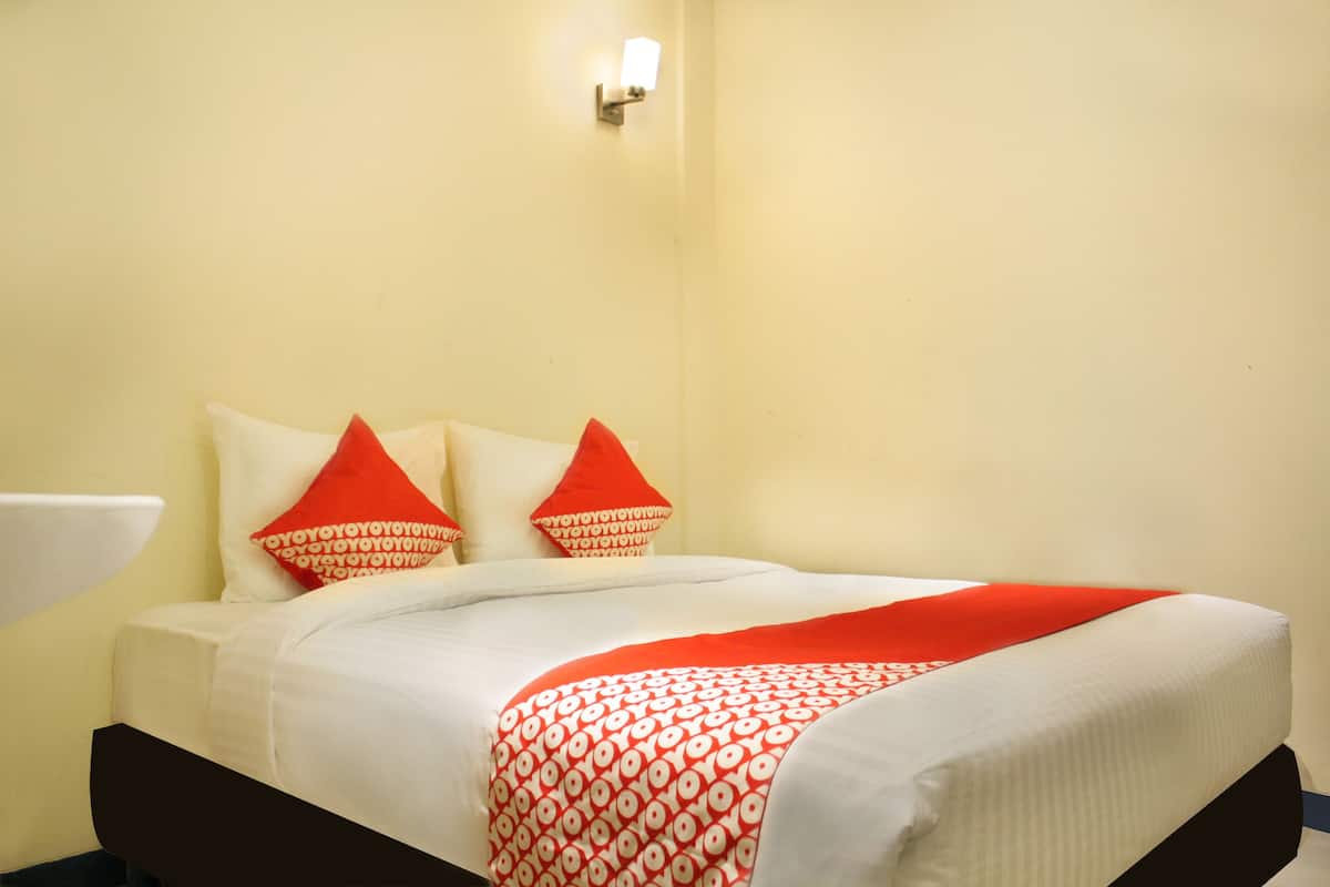 A hotel room with a bed, two pillows, a bedside table, and a wall-mounted light.