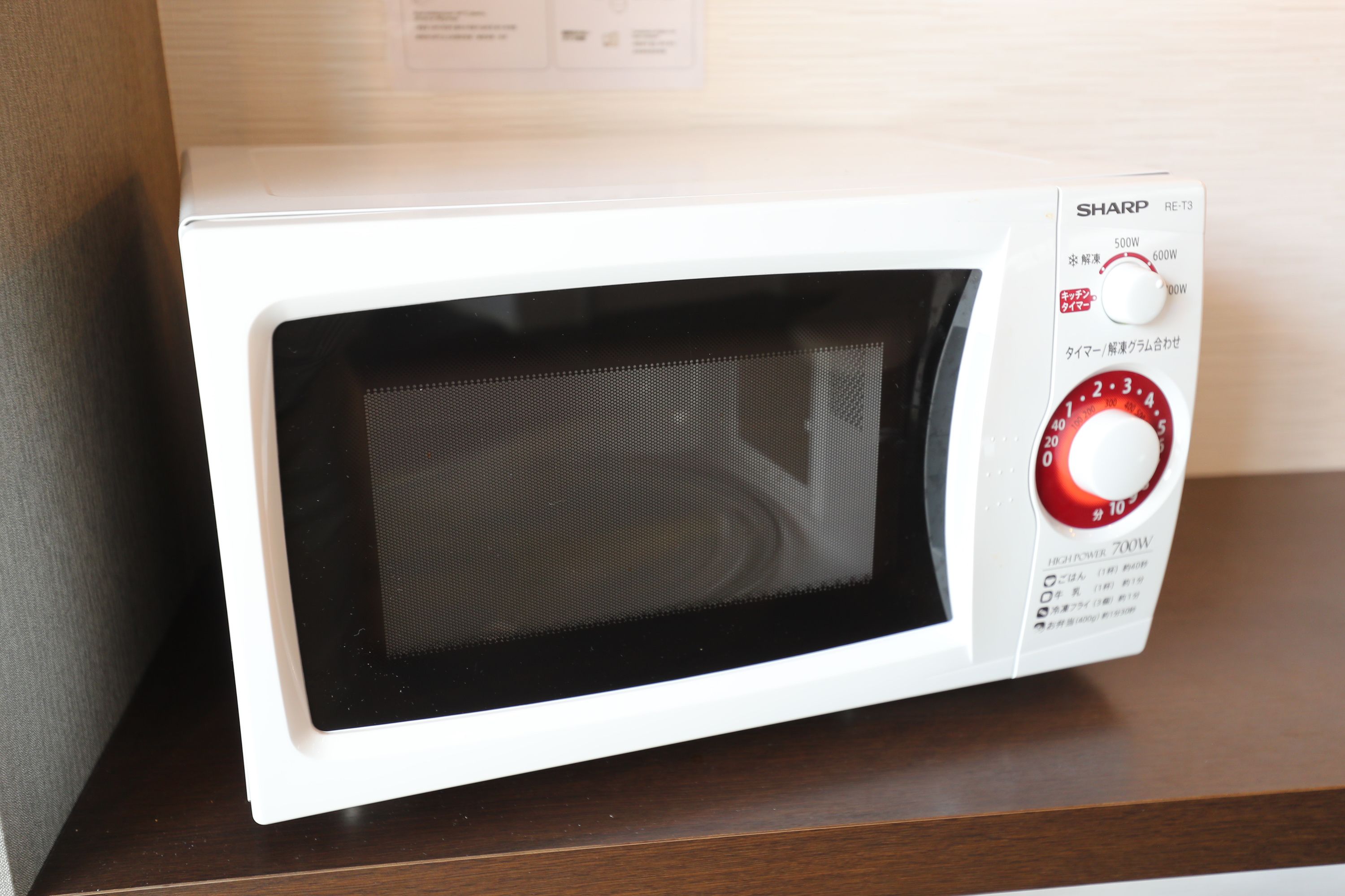 A white Sharp microwave oven with a red dial and a power button, placed on a wooden surface.