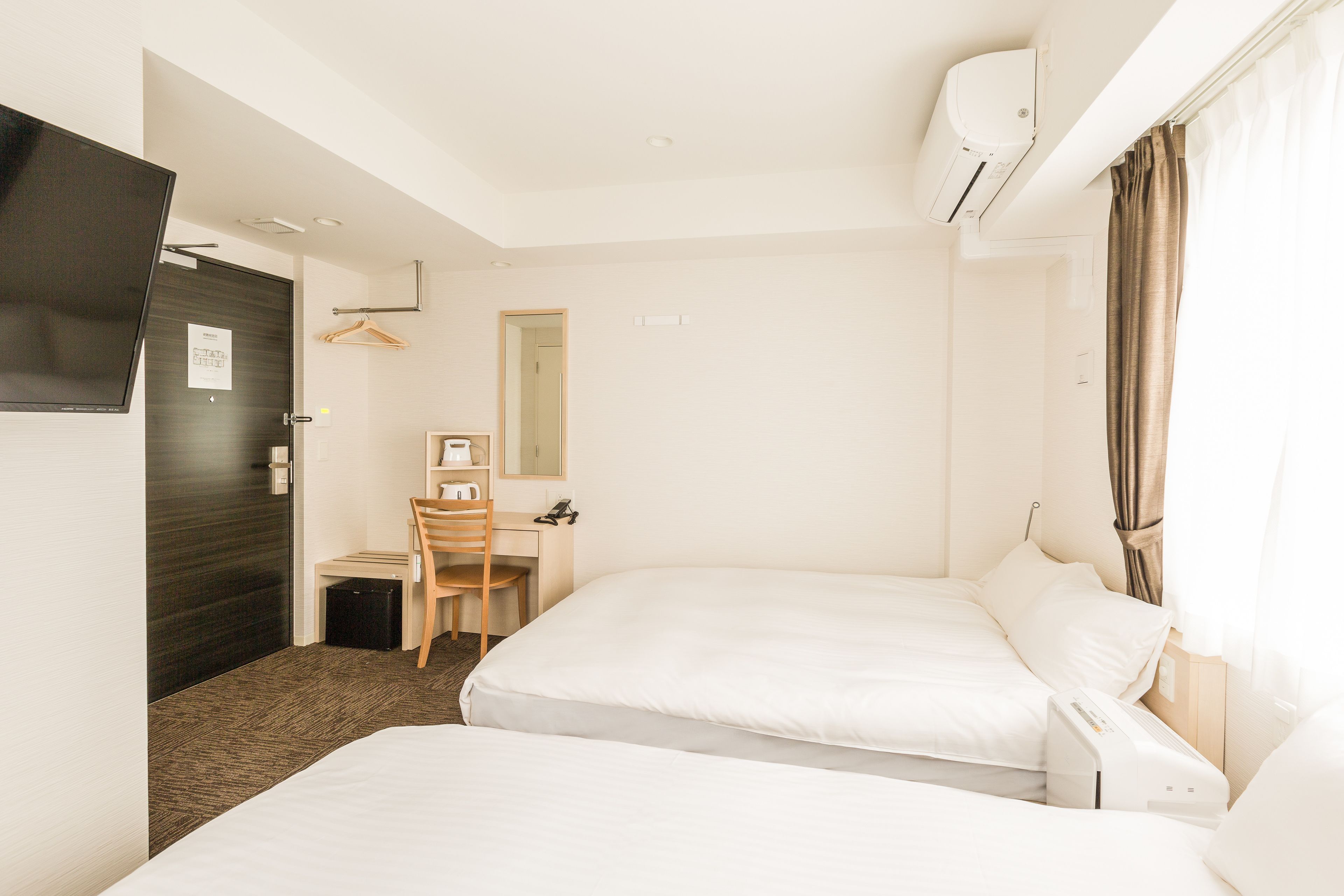 Ett hotellrum med två sängar, ett skrivbord, en stol, en TV och en luftkonditioneringsanläggning.
