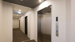 En moderne elevator med kontrolpanel, et tæppe beklædt gangareal og en dør for enden.