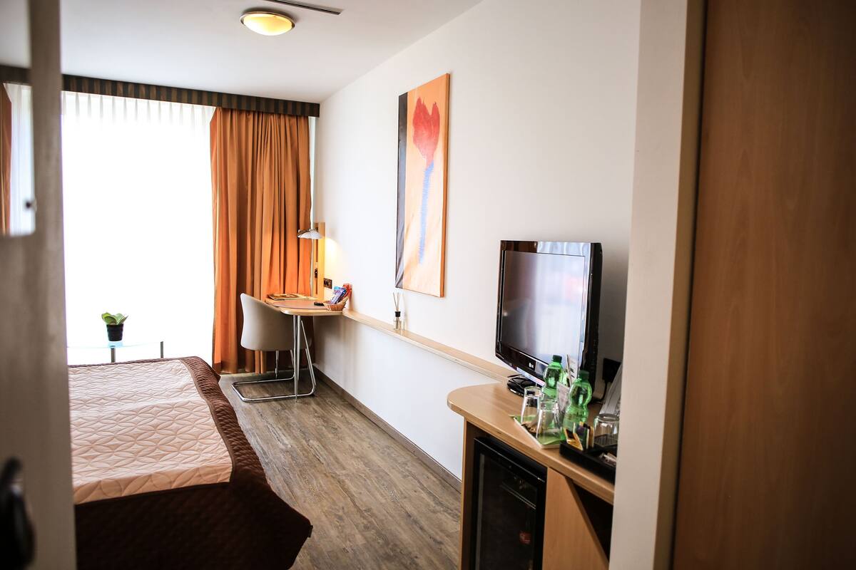 A hotel room with a bed, a desk with a chair, a television, and a wall-mounted artwork.