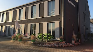 Un hôtel moderne à la façade sobre, doté de grandes fenêtres et d’une enseigne indiquant « Hôtel Arina ».