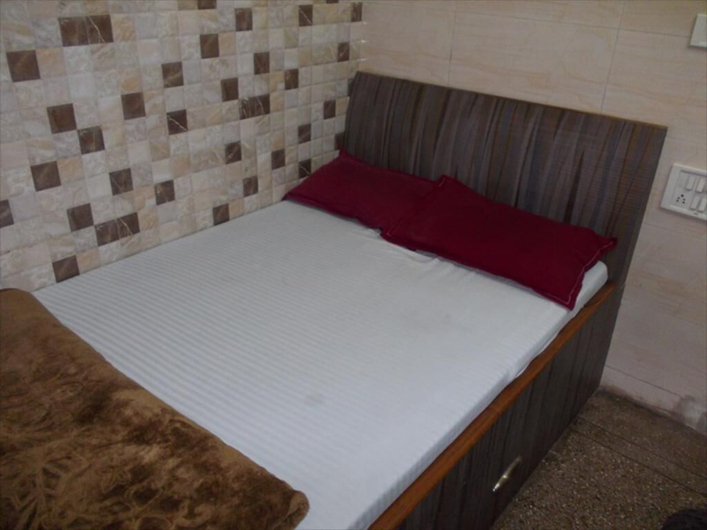 Un lit simple avec un matelas blanc et une couverture marron, un oreiller rouge et une tête de lit à motifs rayés.