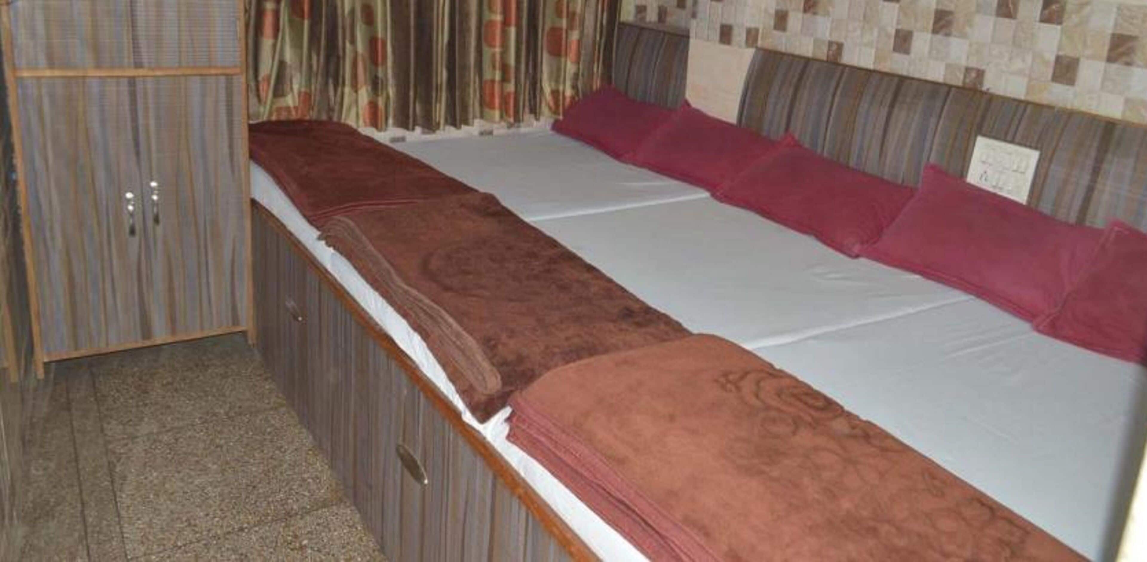 A single bed with a brown blanket and red pillows, a wooden wardrobe, and a patterned headboard.