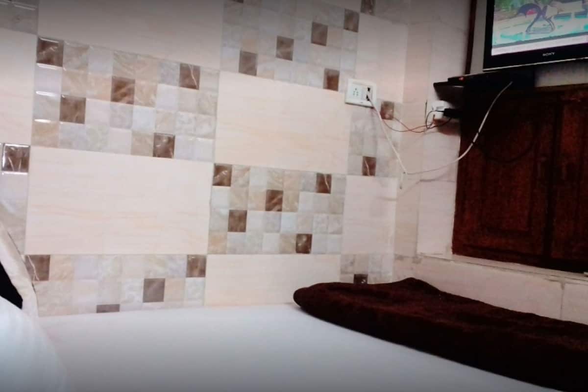 A hotel room with a bed, a TV mounted on the wall, and a tiled wall.