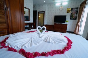 A hotel room with a bed adorned with a heart-shaped arrangement of white towels and pink rose petals, a television, a mirror, and a wooden wardrobe. - Ben Thanh Retreats Hotel (Ho Chi Minh City)