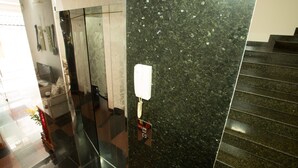 A modern lobby with a marble reception desk, a glass elevator, and a staircase.