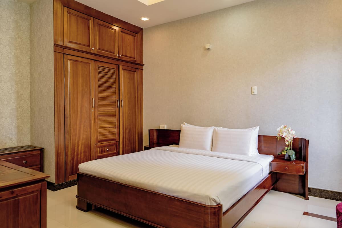 Ein Hotelzimmer mit einem großen Bett, einem Holzschrank und einem Nachttisch mit Blumen.