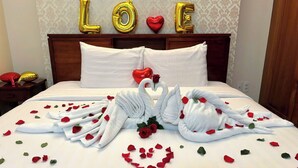 A bed with swan-shaped towels, rose petals, and 'LOVE' balloons on the headboard.