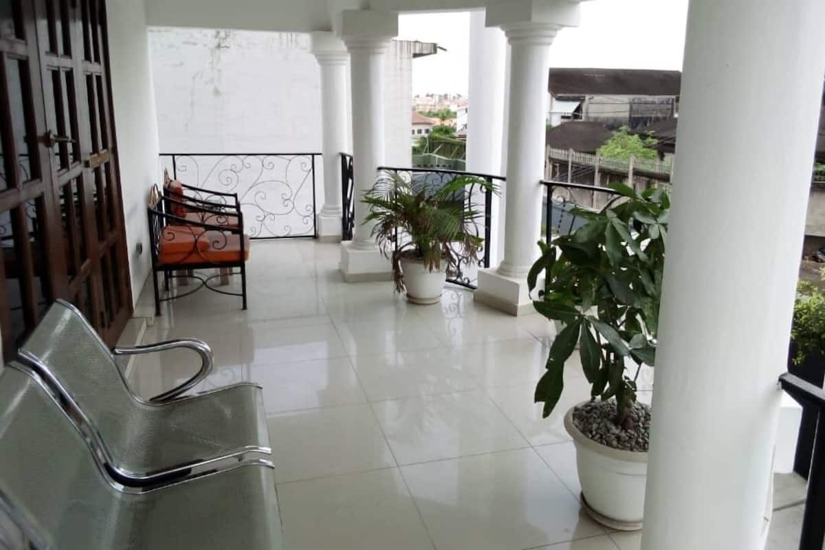 A clean, spacious balcony with white columns, a metal railing, and potted plants.