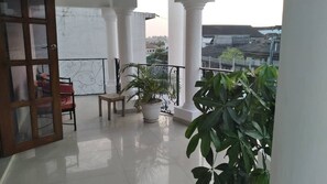 A balcony with white columns, a potted plant, a wooden chair, and a red chair. - Soleil Levant Residence 2 (Abidjan)