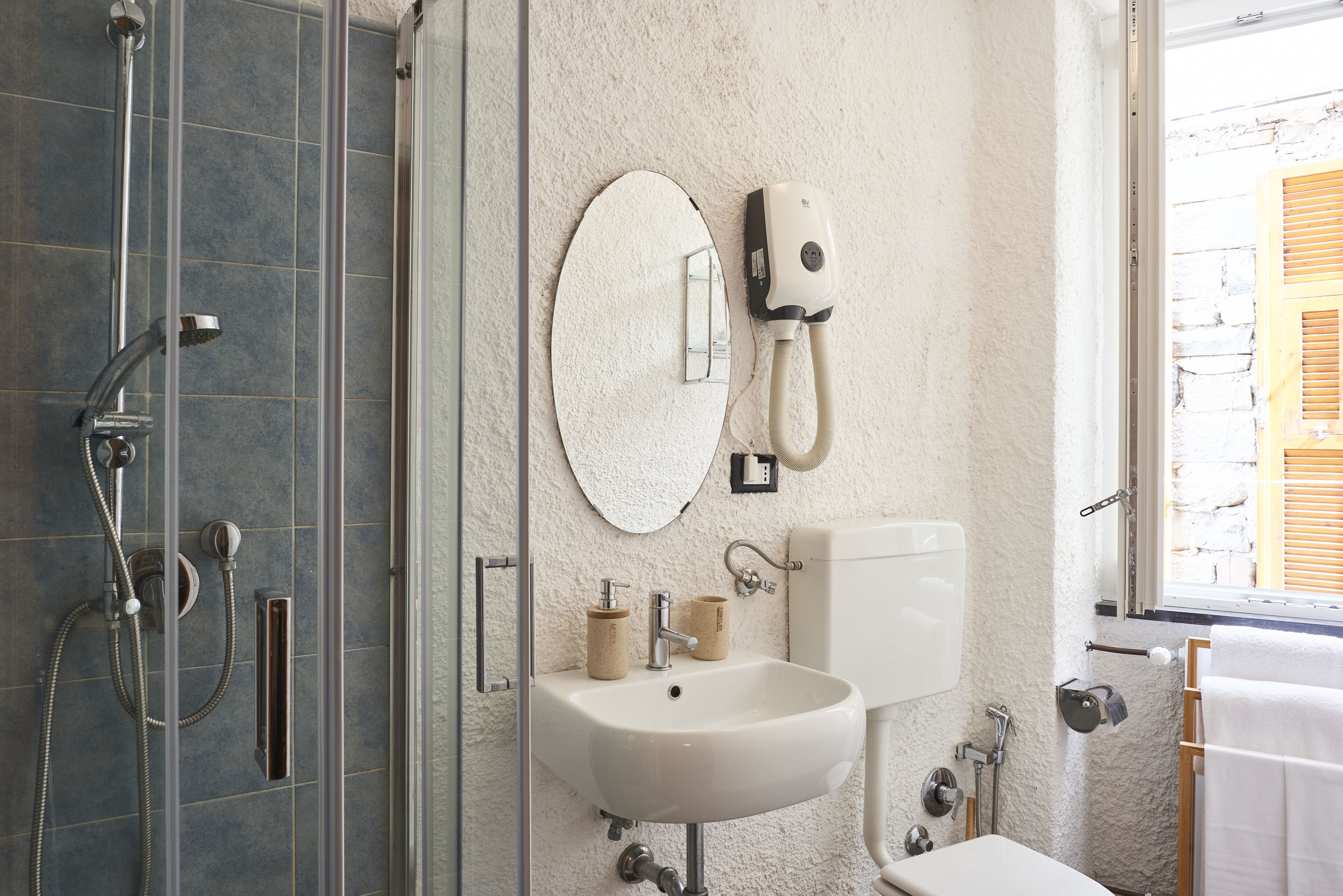 Un baño con ducha de vidrio, un lavamanos blanco, un espejo redondo y un inodoro.