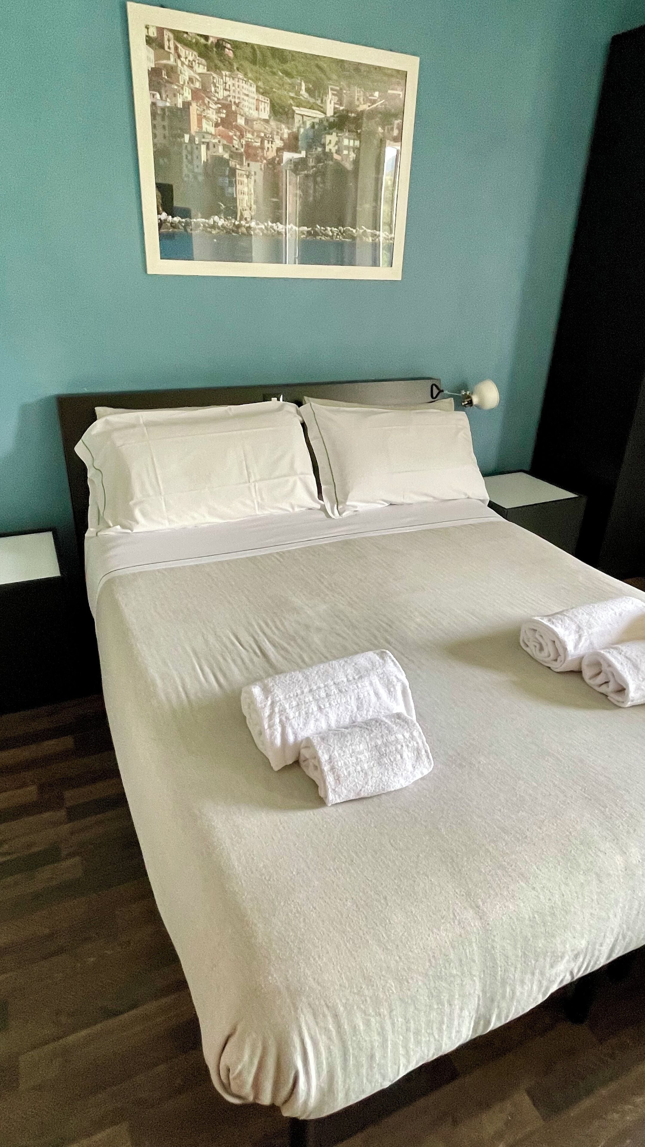 A neatly made bed with white linens and towels, a nightstand with a lamp, and a framed picture on the wall.