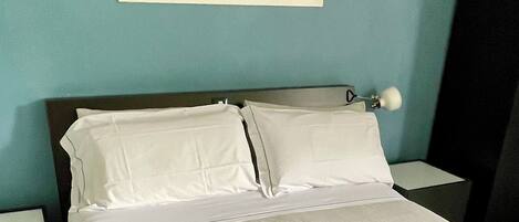 A neatly made bed with white linens and towels, a nightstand with a lamp, and a framed picture on the wall.