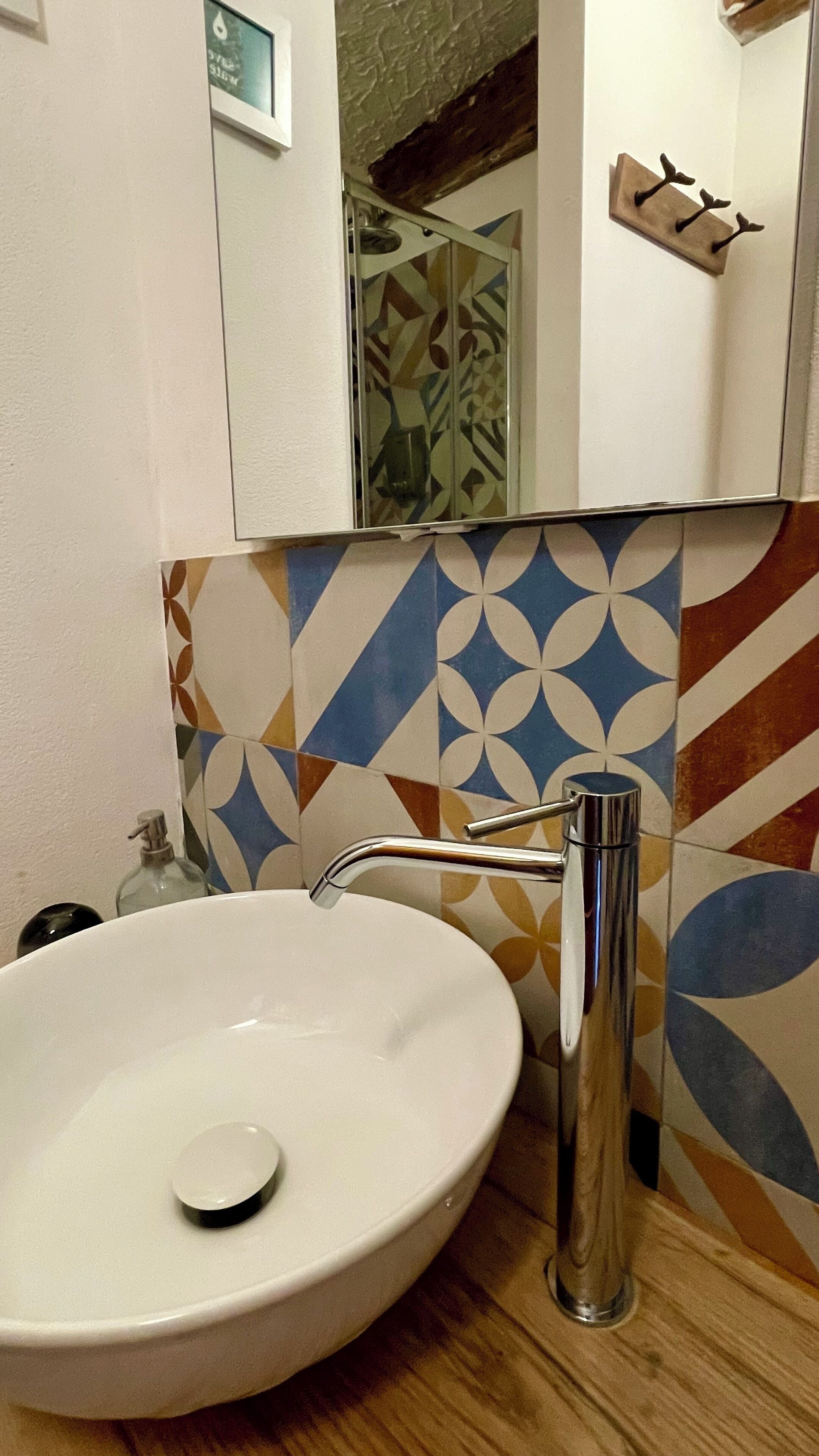 Un baño con lavamanos blanco, un espejo y un salpicadero de azulejos estampados.