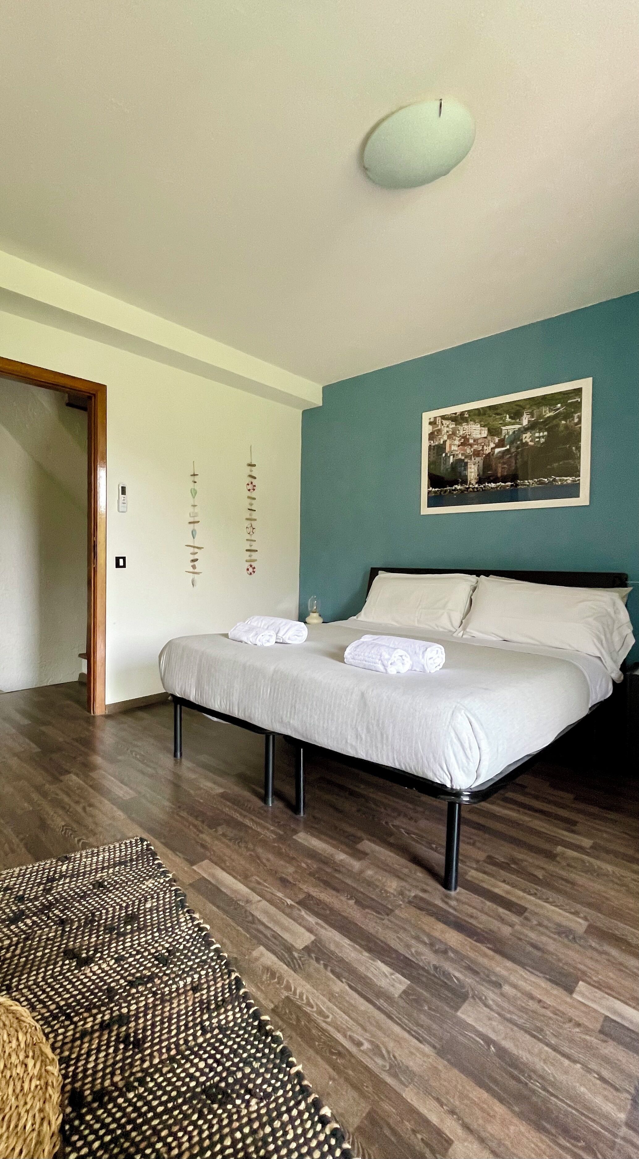 A bedroom with a bed, a painting on the wall, a wooden floor, and a door.