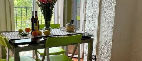 Una habitación con una cama, una mesa con sillas, un televisor montado en la pared y vistas al verde a través de la ventana.