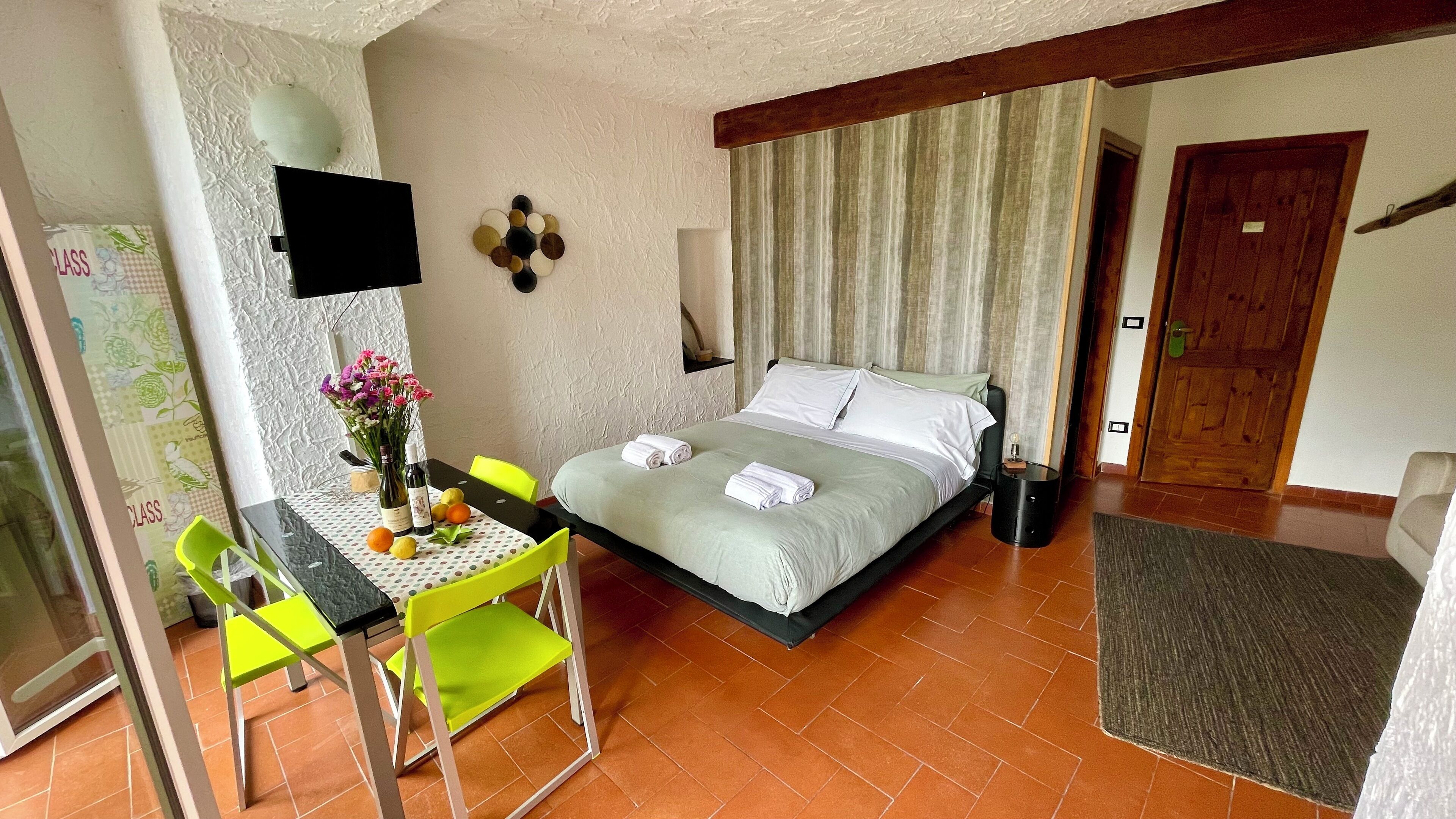 Ein Hotelzimmer mit Bett, Schreibtisch mit Stühlen, Fernseher und einem Fenster mit Vorhängen.
