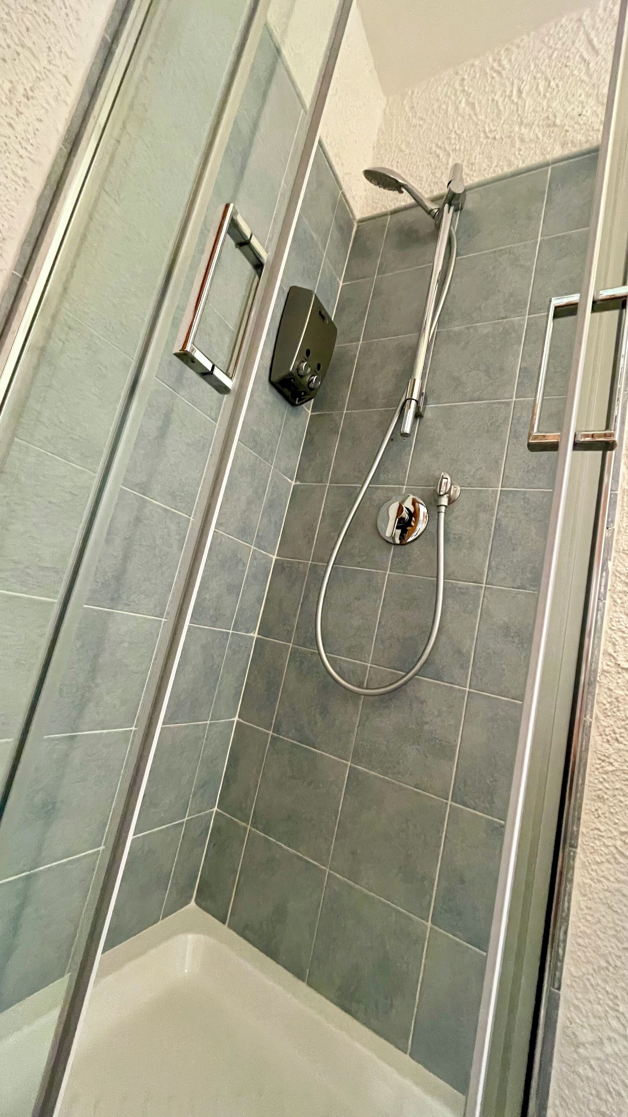 A shower area with a glass door, a handheld showerhead, and a wall-mounted control panel.
